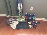 Overview shot with assembled vacuum, accessories, and cleaning solutions on hardwood floor