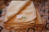 Folded sheepskin mattress cover showing wool pile texture and fabric binding edges. Cream colored folded item laying on patterned bedspread.