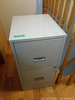 Front view of the 2 drawer filing cabinet showing lock and key on the top drawer, cabinet is light grey metal with label holders on the drawer fronts