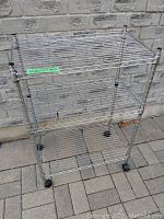 Full view of the metal wire shelving rack with three shelves and casters on the ground.