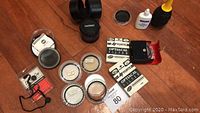 Overview photo showing Tamron zoom lens, 10 camera lens filters in cases, lens blower, and cleaning fluid.