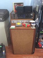 Turntable on wooden cabinet with dust cover, floor speaker with woven fabric front, smaller black Technics speakers on top, plus assorted accessories on floor speaker.