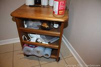 Side angle view of the oak cart showing shelves with various items stored and casters underneath