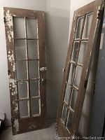 Three old wooden doors with glass panes arranged vertically; doors show chipped brown paint and original metal hardware.