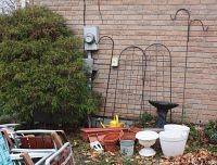 Wide view of lot showing lawn chairs, trellises, birdbath, planters and watering can against brick wall
