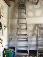 Full front view of the 10 foot aluminum step ladder in a storage area, showing its full height and step layout.