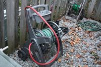 Plastic garden hose reel cart with green hose wound on it and red hose included. Tool caddy shelf on top and wheels for portability.