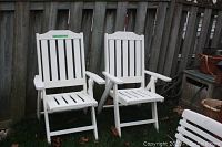 Two heavy duty white outdoor captain chairs with vertical slats, armrests, and solid sturdy frames placed on grass near a fence.