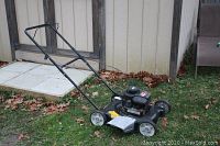 Side view of black Briggs and Stratton Yard Machines push mower on grass near a shed, showing deck, wheels and handlebar.