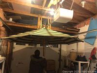 Photo showing full view of the open patio umbrella inside a garage, featuring a striped canvas canopy and wood frame.