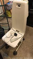 Front view of the white battery-operated bathtub lift chair with attached remote and battery charger.