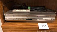 Front view of Samsung DVD VHS combo player showing remote on top, cords behind, lot number 214