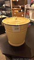 Full view of the yellow enamel bucket with lid on top, showing its smooth finish and round shape.