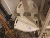 Side view of white plastic bath chair showing seat, backrest with cut-out handles, and partial adjustable leg visible.