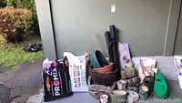 Wide view showing all items including bags of potting soil, planters of various materials, watering cans, and black cloth.