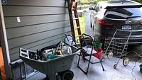 Photo of assorted ladders, stools, buckets, grocery cart, and wheelbarrow on porch area