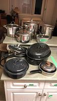 Full lot view showing various pots and pans including large pasta pots, frying pans, turkey pot and small pans on kitchen counter.