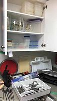 Kitchen cabinet interior with stacks of plastic storage containers and plastic drinking glasses, some decorated with designs.