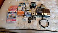 View of all items in the lot arranged on a bed; six clocks including Timex, Sony, and General Electric models, Conair foreign electrical plugs, a wall timer, and packages of vacuum space saving bags