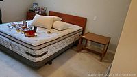 Wide view of bed with mattress, headboard and frame, plus bedside table and dresser showing context in room
