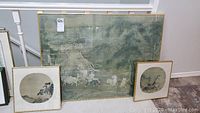 Three framed prints leaning against stair railing: one large rectangular and two small circular prints