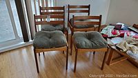 Four teak side chairs arranged in room with bamboo flooring, each topped with olive green cushions.