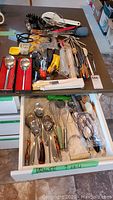 Overview of assorted kitchen utensils including spoons, whisks, basters, wooden spoons, and other cooking tools laid out on a table.
