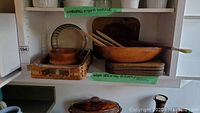 Shelf display of the glass casserole dish and wooden tray, wooden salad bowl, placemats, and mixing forks.