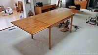 Overall view of fully extended teak dining table with rolled edge and tapered legs