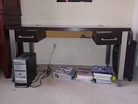 Front view of computer desk with two drawers and missing middle drawer. Desktop PC tower is underneath the desk.