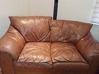 Front view photo of the brown leather loveseat showing the seating area, cushions, armrests, and visible slight indentation on the right side.