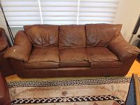 Front view of 7-foot brown leather sofa sleeper showing tear on right armrest and three seat cushions.
