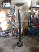 Full view of the halogen floor lamp standing in a garage or storage space with various tools and items on shelves around.