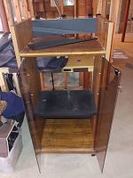 View of wooden audio component storage unit with lower glass doors open revealing shelves inside. The unit is on caster wheels and has a mesh shelf near the top.