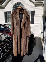 Full-length front view of woman’s raccoon fur coat held up outside showing natural brown fur color and texture.