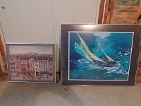 Photo of two framed art prints. Left: 'French Scene' by Delacroix depicting a French townscape with buildings and people, framed in silver. Right: 'Regatta' by Leroy Neiman showing a sailing scene with bright colors and dynamic brush strokes, framed in black with navy blue mat.