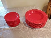 Two stacks of bright red ceramic plates on table, larger dinner plates and smaller salad plates