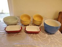 Photo showing assorted colourful serving dishes on table: 3 yellow bowls stacked, 2 small rectangular red and white dishes, 1 large blue bowl, 1 large light blue bowl with geometric pattern.