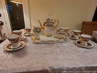 Full set arranged on table showing tray, teapot, sugar bowl, creamer and four cup-and-saucer sets.