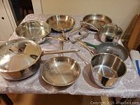 Photo showing multiple pots and frying pans including Oneida, Paderno and Le Creuset cookware on a table.