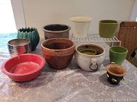 Eleven assorted flower pots displayed on a table showing colors, sizes, and shapes of each pot.