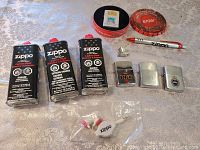 All Zippo lighter fluid cans, Zippo lighters, pen, and accessories displayed on table with clear detail of labels and paintwork