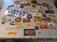 Photo showing assortment of 30+ colorful embroidered patches spread on lace tablecloth, sports and organizational themes visible