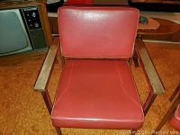 Close-up photo of one vintage office chair showing red vinyl upholstery and solid wood armrests.