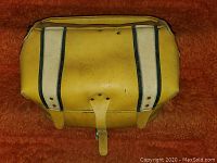 Yellow genuine leather Bombardier snowmobile saddle bag with black vertical stripes and buckle strap closure, resting on rust-colored fabric surface.