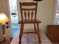 Front view of one wooden chair showing turned legs, spindle back and wooden seat.