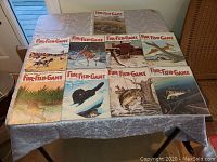 Full set of nine Fur-Fish-Game magazines laid out on a table showing all front covers with wildlife illustrations including birds, mammals, and fish in natural outdoor scenes.
