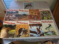 All nine Fur-Fish-Game magazines laid out on a table displaying their wildlife illustrated covers.
