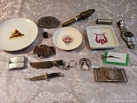 Photo showing wide view of all lot items including the ring, knives, belt buckles, whistle, watches, and collector plates.