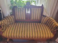 Front view of vintage settee couch with striped upholstery and wooden arms.